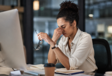 Burnout silencioso: mulher exausta no ambiente de trabalho segura os óculos enquanto demonstra sinais de cansaço emocional e esgotamento profissional diante do computador.