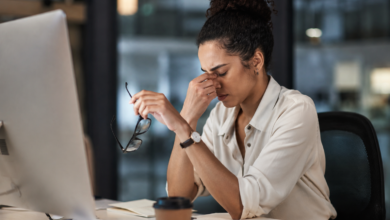 Burnout silencioso: mulher exausta no ambiente de trabalho segura os óculos enquanto demonstra sinais de cansaço emocional e esgotamento profissional diante do computador.