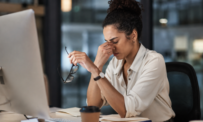 Burnout silencioso: mulher exausta no ambiente de trabalho segura os óculos enquanto demonstra sinais de cansaço emocional e esgotamento profissional diante do computador.